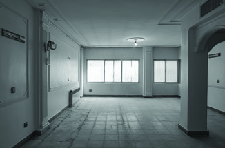 Before renovation: empty room of the original apartment with tiled floor, arched openings, and windows to the garden