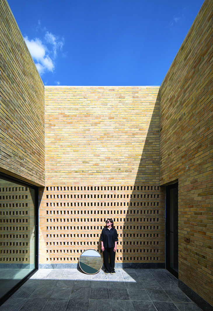 Central courtyard enclosed by tall brick walls with a perforated brick screen, a woman standing with a round mirror, open to the sky above