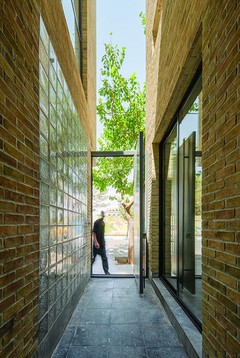 Interior corridor with brick and glass block walls looking out toward the garden through a full-height glass door