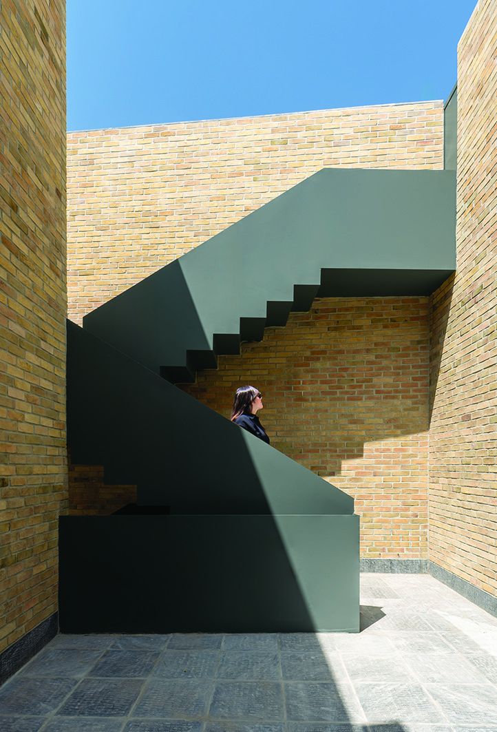 Exterior green metal staircase in the brick courtyard, with a woman sitting on the stairs looking up at the sky