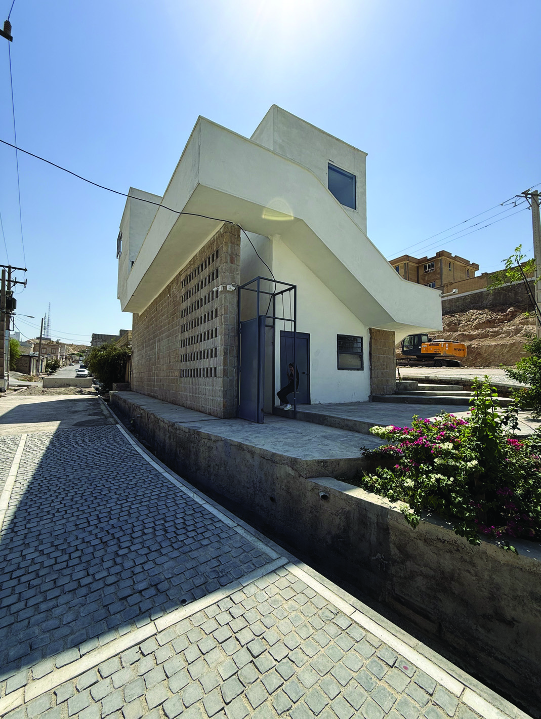 Close-up of the entrance level with hewn stone block walls, white concrete canopy, a glass entrance door, and a bougainvillea bush in the foreground