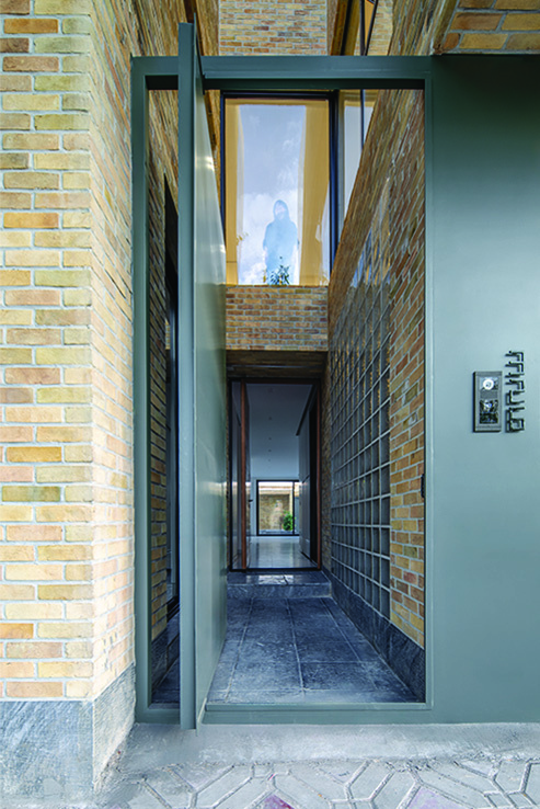 Narrow entry hallway with a glass pivot door, brick walls, glass blocks, and daylight from above