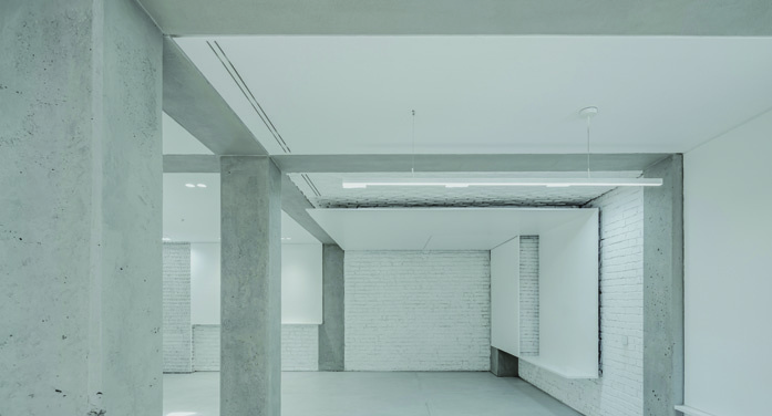 Exposed concrete ceiling with beams and columns, whitewashed brick wall, a recessed ceiling light, showing the raw materiality of the original structure