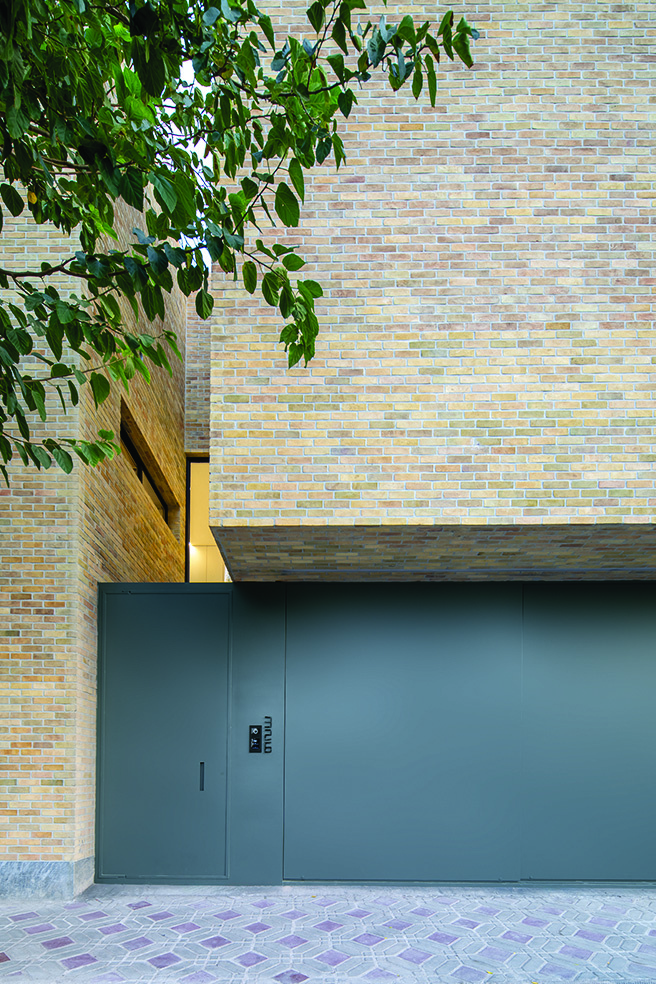 Detail of the multi-coloured brick facade with the dark green metal entrance gate and stone paving