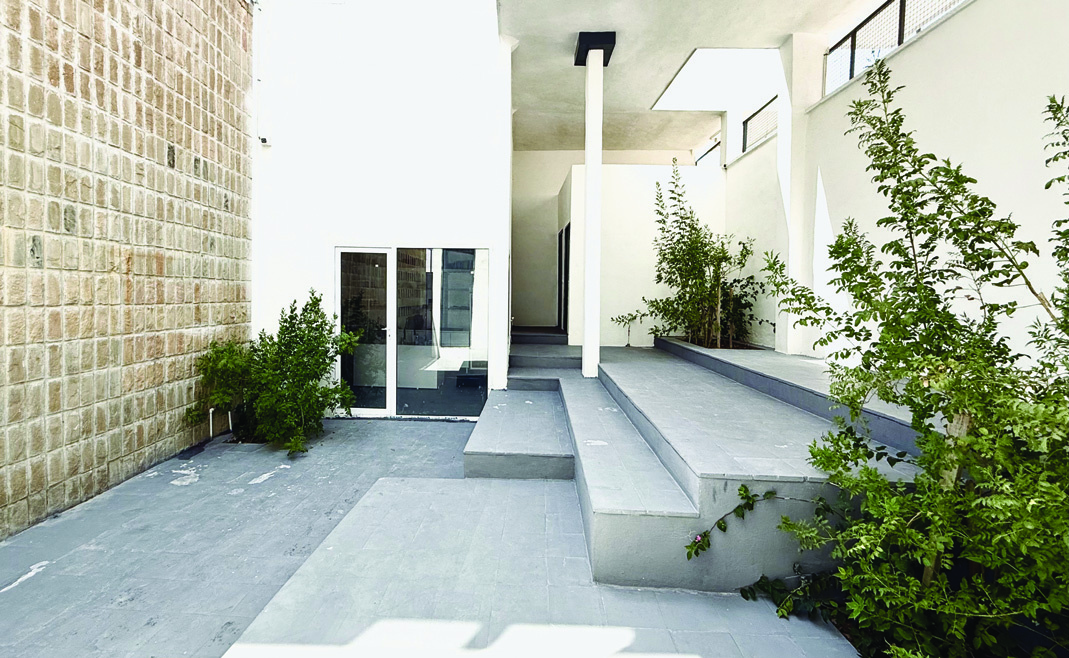 Ground floor area with a glass entrance door, stone wall, white concrete walls, green plants, and stepped platforms