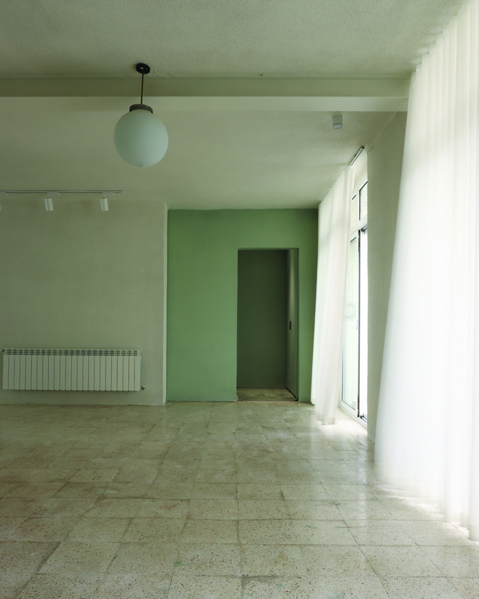Interior room with soft green walls, a pendant globe light, track lighting, sheer curtains billowing with breeze from the courtyard window