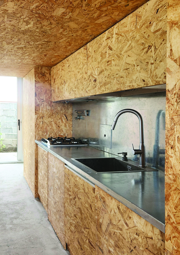 Kitchen interior clad entirely in OSB panels with stainless steel countertop, gas hob, and modern faucet