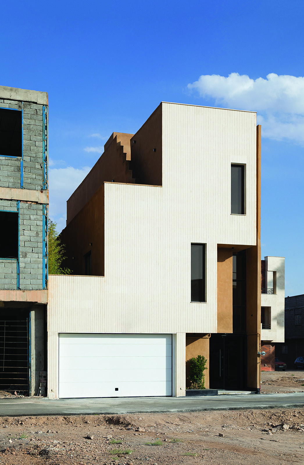 Nim Rokh main facade in daytime &mdash; white corrugated cladding with earth-toned stepped volumes, small windows on upper floors, white garage door at ground level