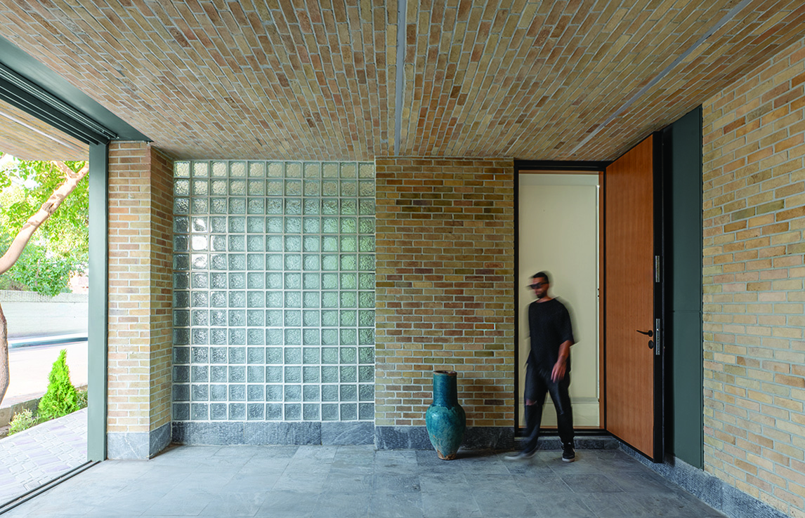 Interior of the covered parking area with exposed brick ceiling, glass block wall, person entering through wooden door