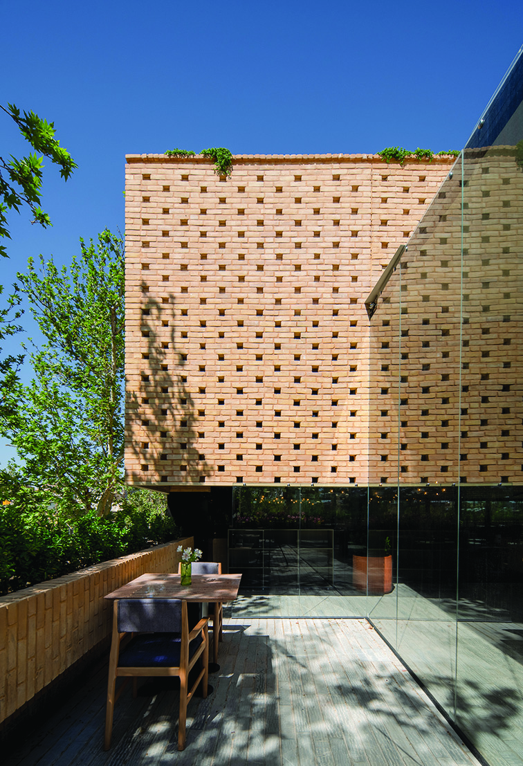 Rooftop terrace with perforated brick screen wall, wooden decking, glass balustrade, a table and chairs, greenery on top of the wall