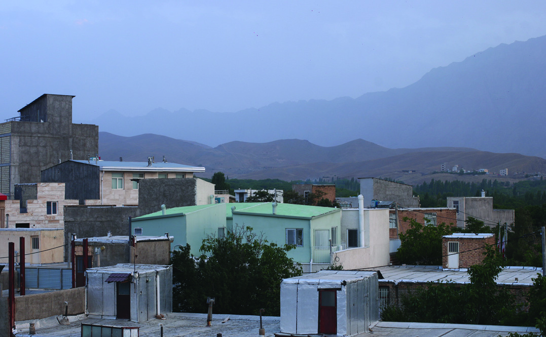 View over the rooftops of Khansar at dusk showing the green-roofed Khan Khaneh house amid the town fabric, mountains receding into mist behind