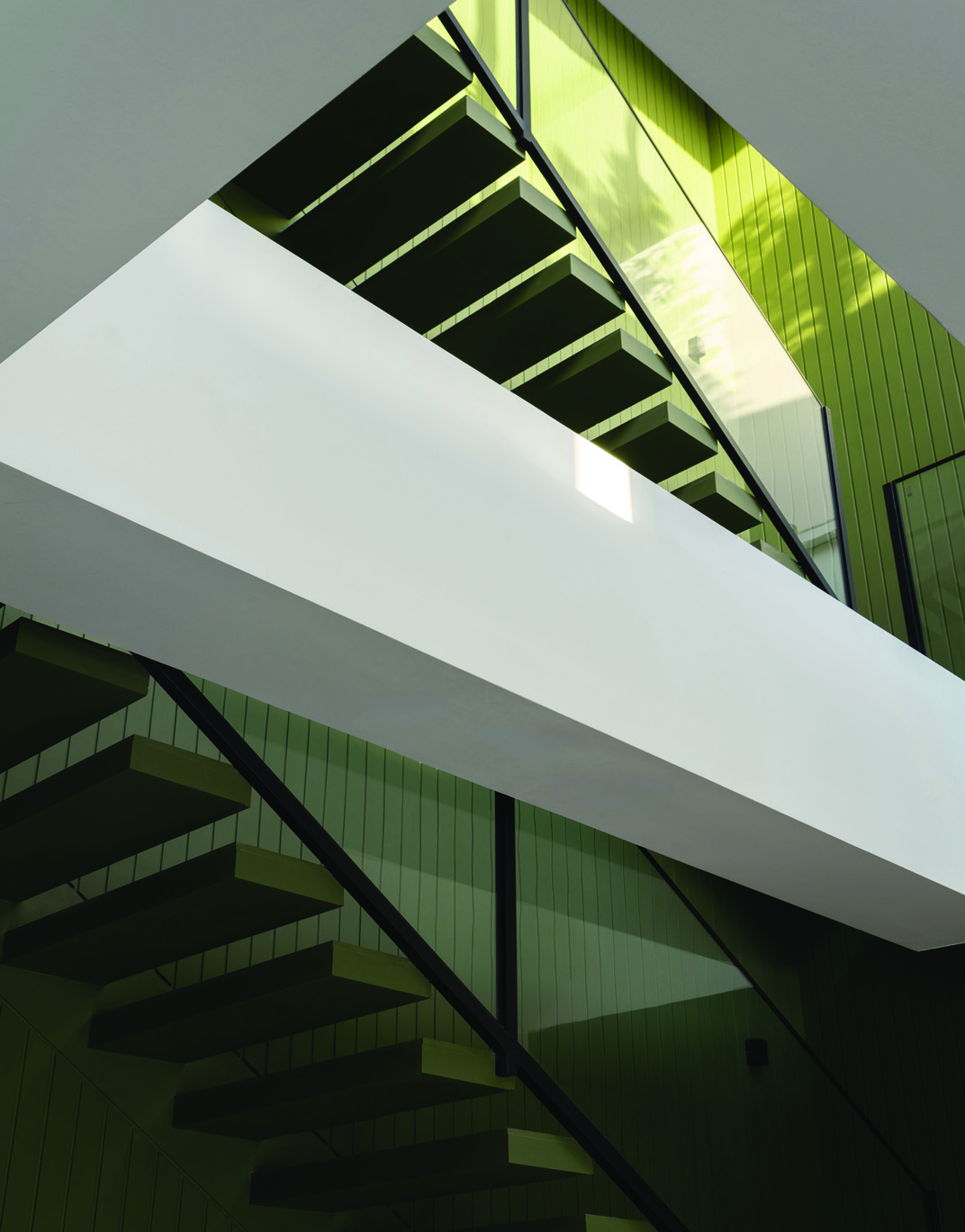Angular view looking up through two flights of floating stairs against green-panelled walls, geometric composition of treads and glass balustrades