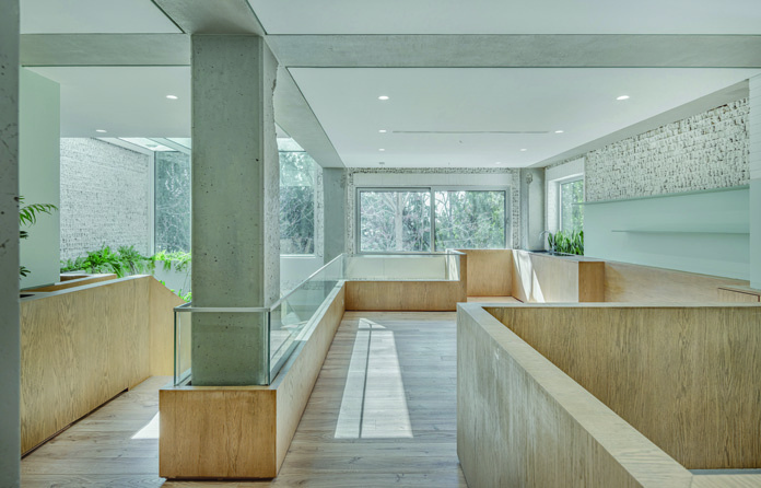 Upper level gallery with wooden flooring and oak balustrades, concrete columns and beams exposed, windows on multiple sides allowing views of the garden