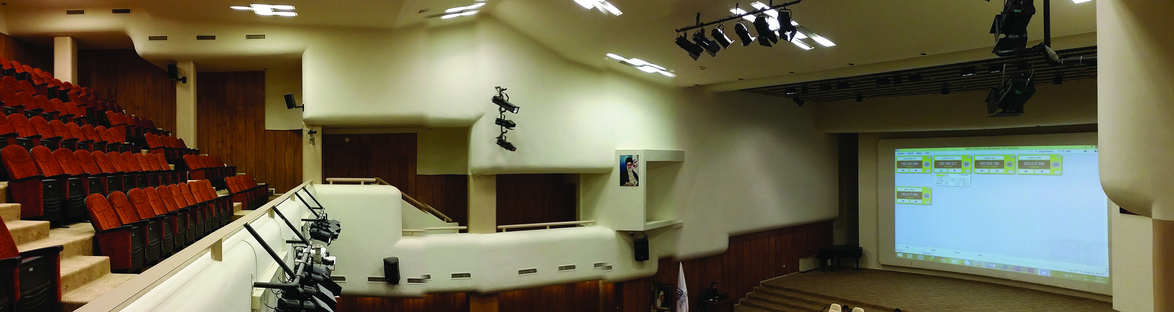 Conference hall interior showing auditorium seating, projection screen, and stage