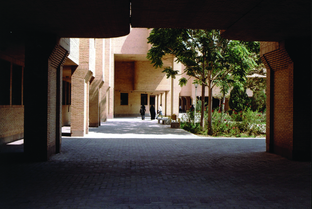 View through a brick archway into an inner courtyard with lush garden and trees