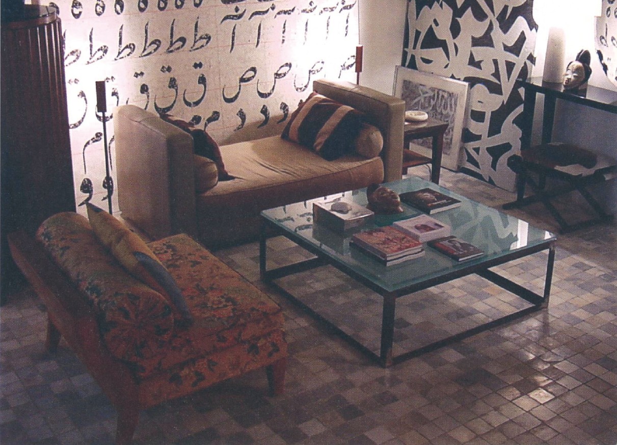 Living room with calligraphy-painted wall: Farhad Moshiri large-scale painting, Zenderoudi small work on paper, leather-and-velvet day-bed, walnut drinks cabinet, L-frame metal coffee table with sand-blasted glass top, sofa, floor lamp, lacquered side-table, African mask, recuperated Yazdi 'ZILU' cushions