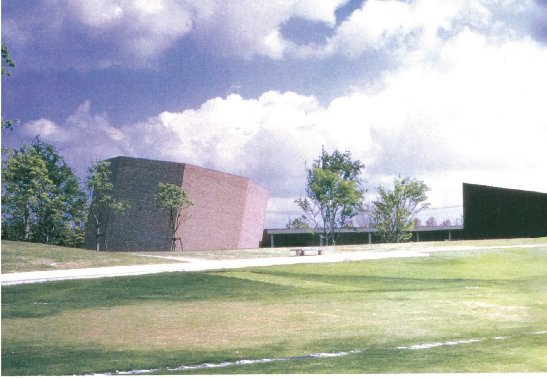 View across the grass meadow toward the long, low brick volumes of the Kaze-No-Oka crematorium complex