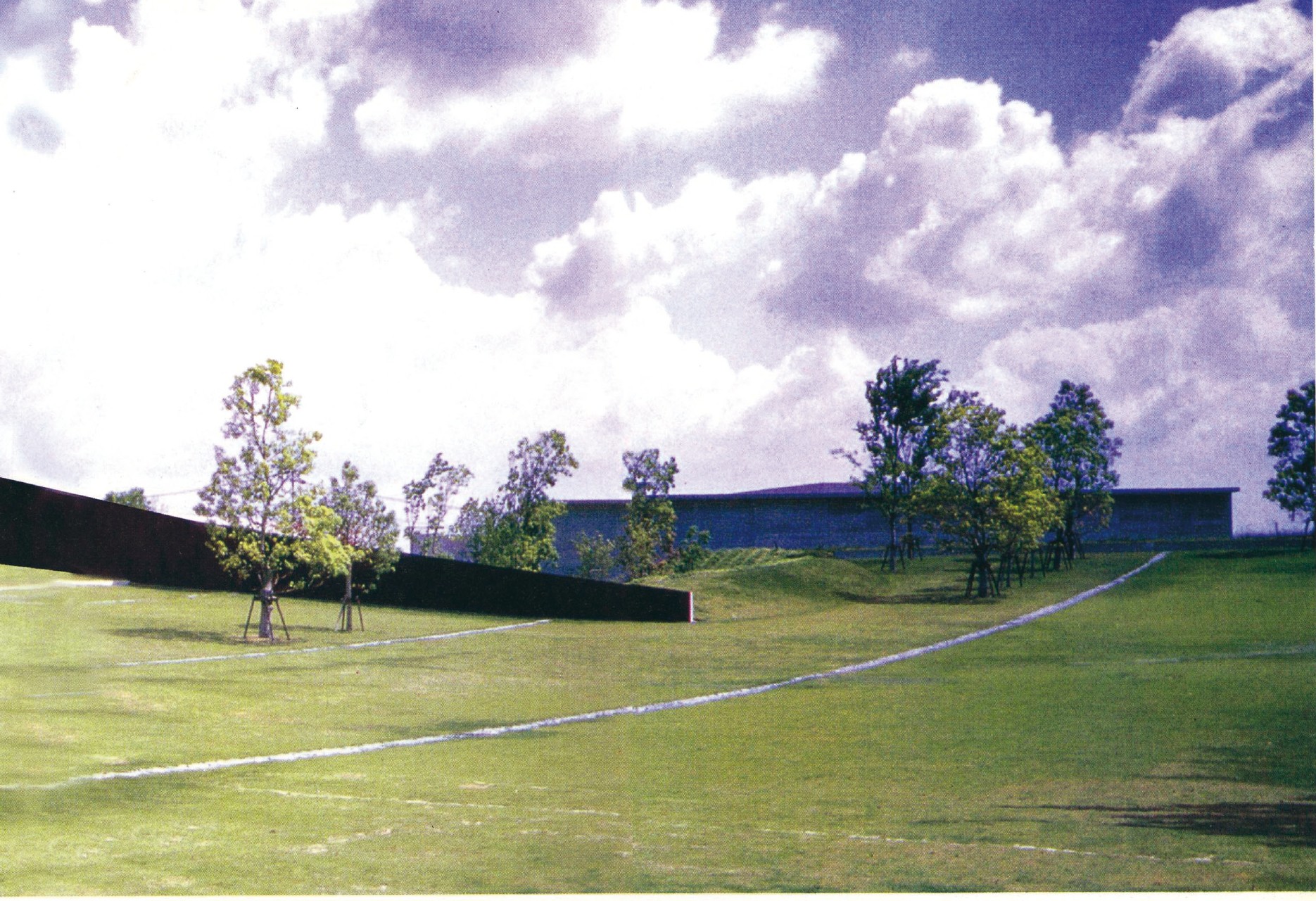 Wide-angle view of the Kaze-No-Oka (Wind Hill) crematorium grounds in Oita, Japan, low concrete walls and metal roof set into a wooded hill