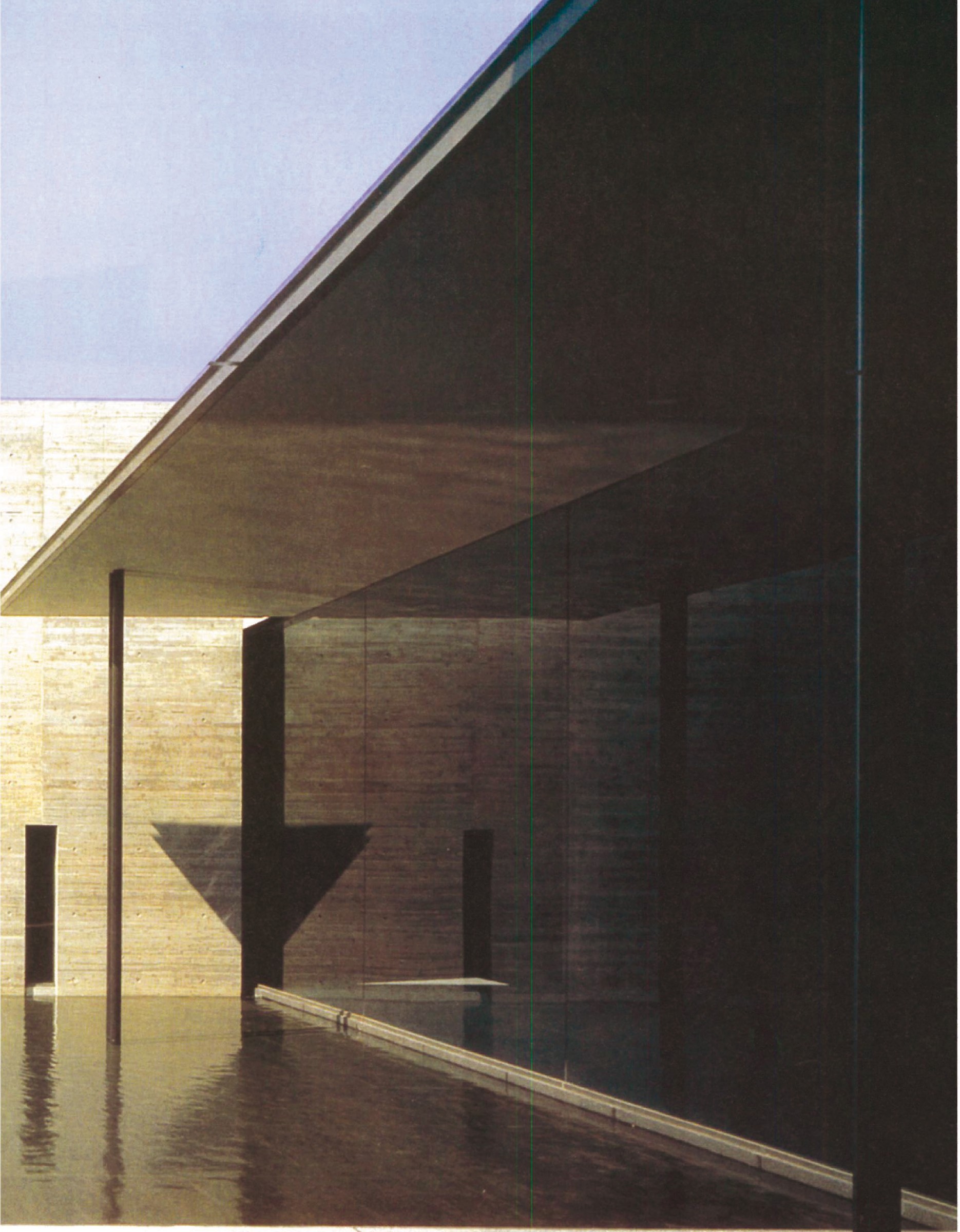 Reflecting court of the Kaze-No-Oka crematorium at dusk: long planes of dark concrete frame a still pool, with a single light V-shaped vertical accent rising at the back