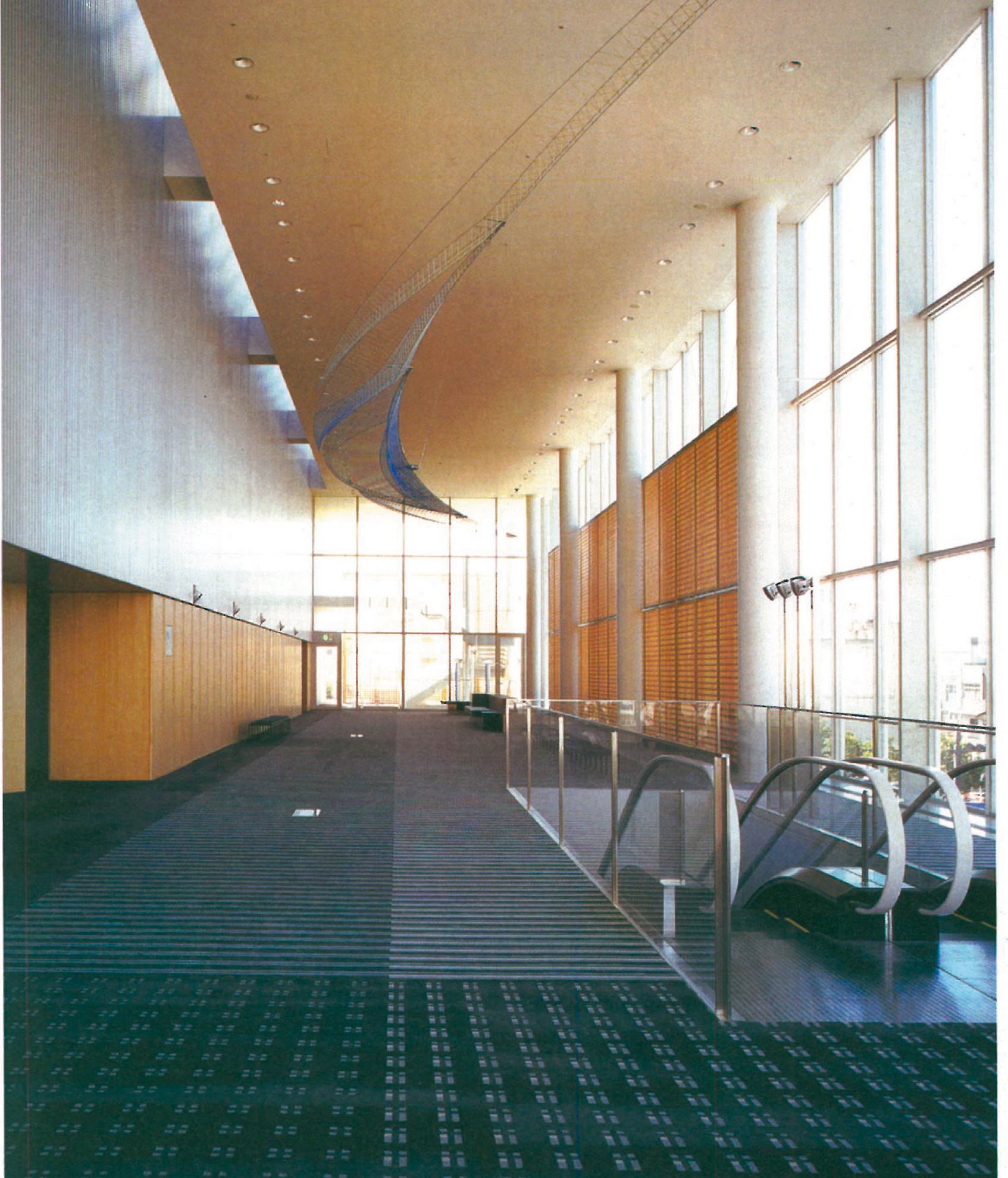 Main foyer of the International Gatherings Center in Toyama, Japan — long curved wall of warm wood and glass receiving daylight through clerestory windows