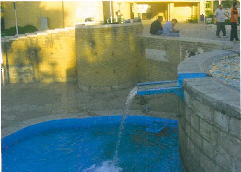Detail of a curving water channel through Niavaran Park — the cut-stone gutter edge painted bright blue, contrasting with the brick paving and stone-clad parapet.