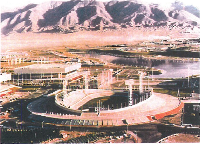 Aerial view of Azadi Stadium in Tehran by Aziz Farmanfarmaian — oval bowl with floodlight masts, the adjacent indoor arena, and the Alborz mountain range rising in the background