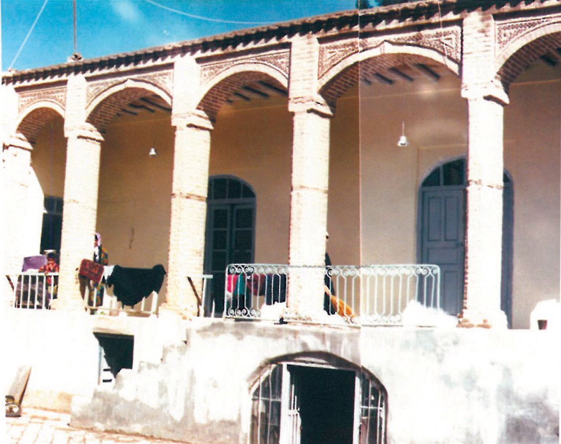 Courtyard view of Example 7 in the Birjand survey: a two-storey arcade of slender columns supporting brick arches with hung textiles drying in the courtyard