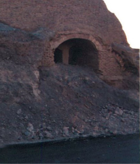 An old conical adobe ice-house (yakhchal) in Birjand with a vaulted entrance opening at its base, set against a barren earthen mound