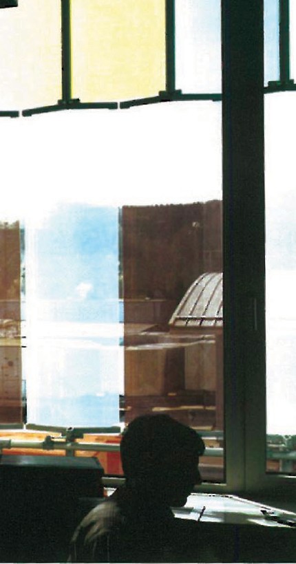 Boehringer Ingelheim laboratory interior — open hall lined with coloured glass-brick panels in red, orange, yellow and pink across full-height window bays, exposed steel structure overhead