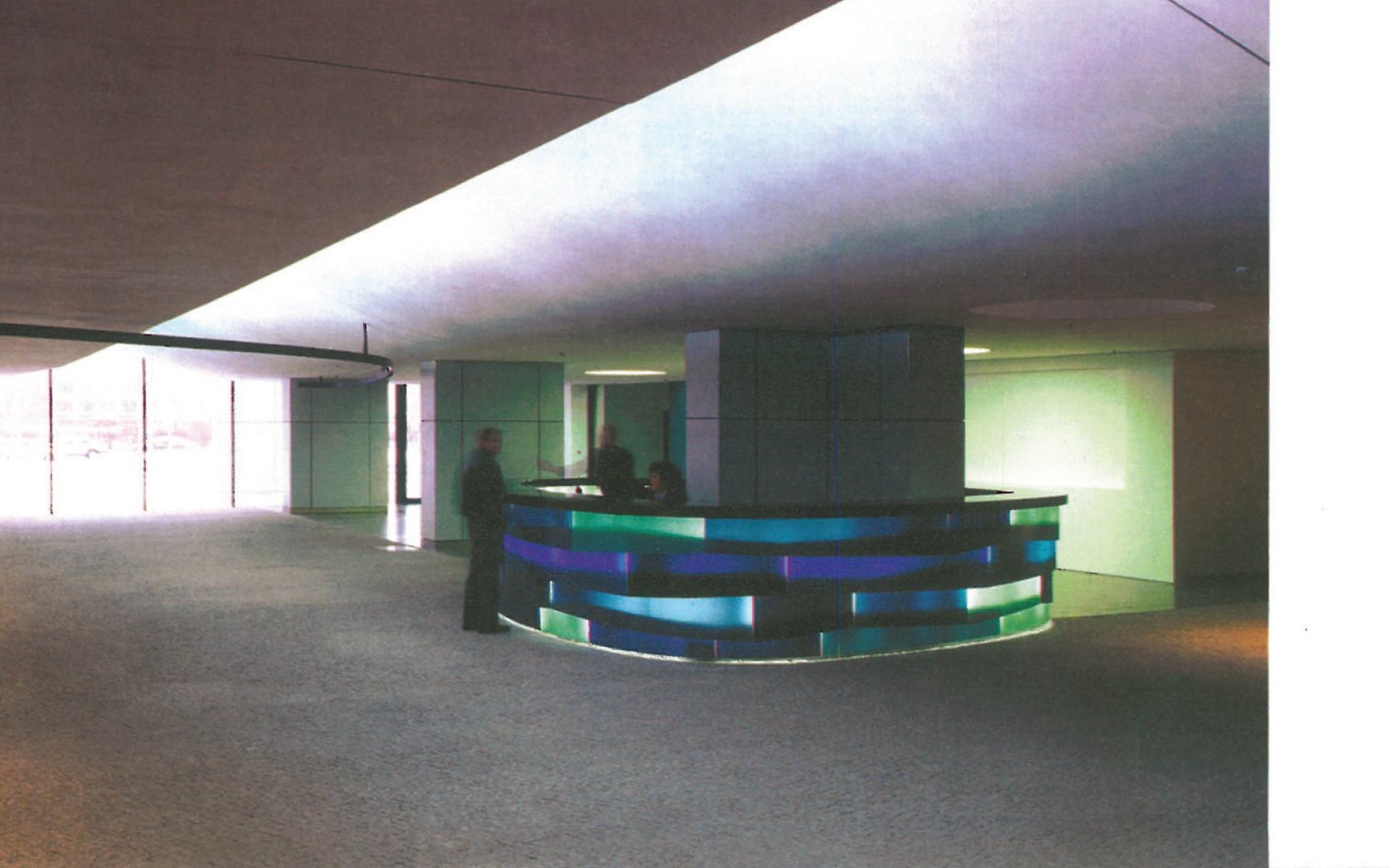 Reception lobby of GSW Headquarters Berlin — softly curved white ceiling above a freestanding circular reception desk lit from within by horizontal bands of green, blue and pink