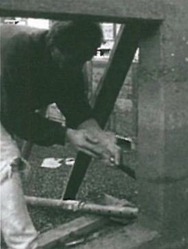 Worker reaching into a curved prefabricated rammed-earth wall panel for a private house in Nuziders, with the fireplace emplacement preserved within the form