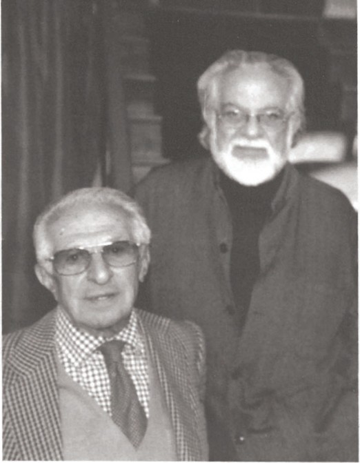 Black-and-white editorial portrait of architects Mohammadreza Moghtader (seated, in tweed jacket and tie) and Abdolaziz Farmanfarmaian (standing, in dark jacket with white beard) photographed together