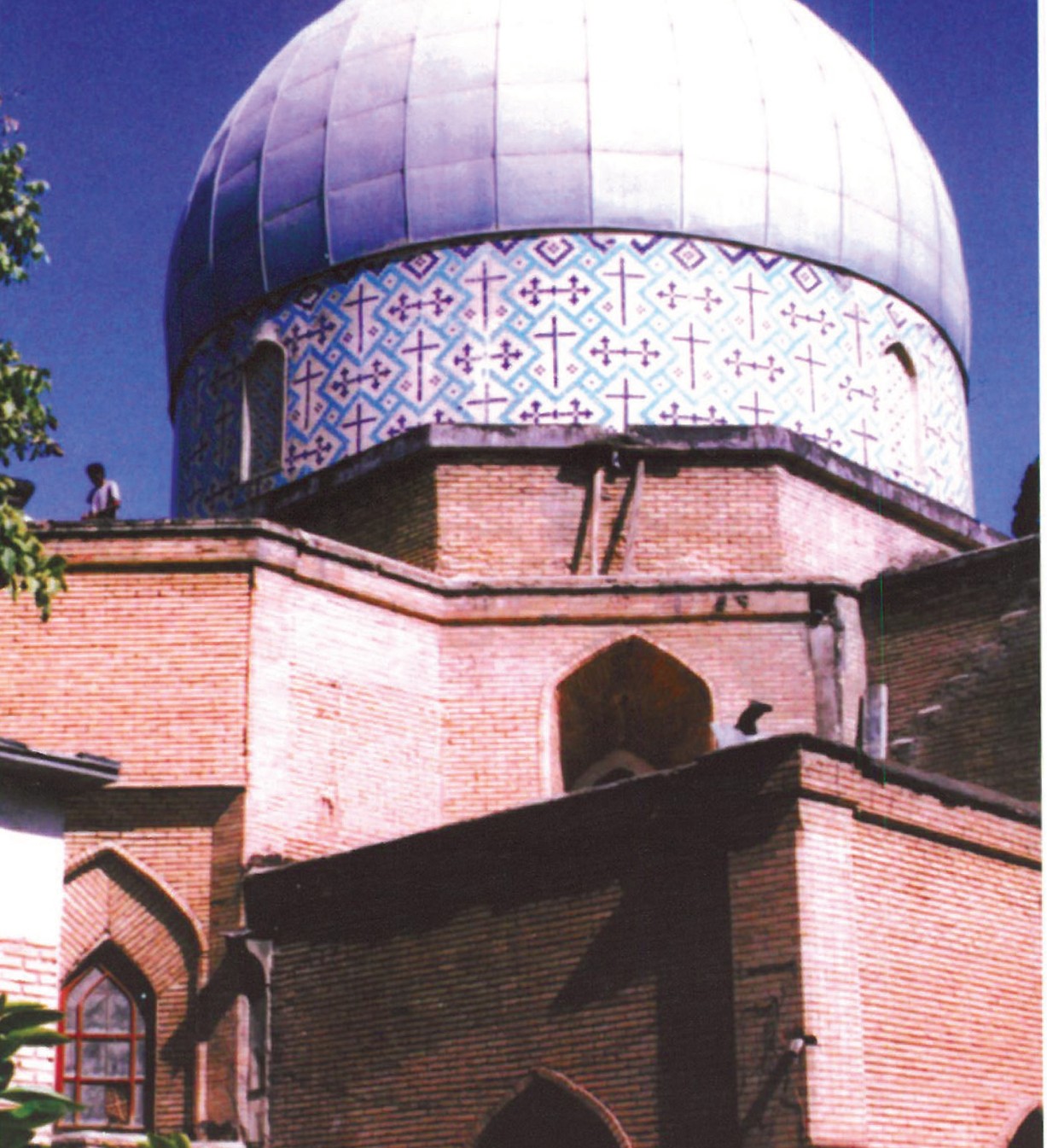 Hero photograph of the Armenian church courtyard near the priest's house in Shiraz — domed brick rotunda with blue-and-white scaled cupola rising above brick gables, with a smaller octagonal pavilion in the foreground