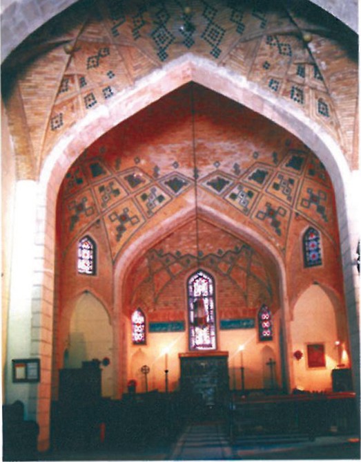 View through the church nave toward the painted altar arch — slender pointed arches frame a deeply decorated apse beyond