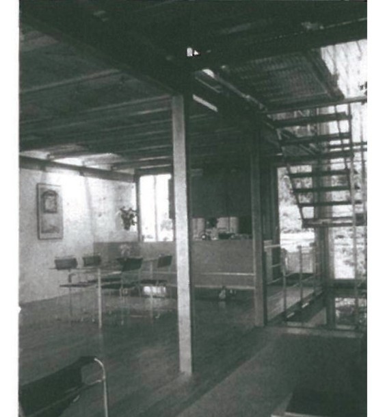 Interior of Günther Domenig's Neufeldweg residential building in Graz (1984-1988) — angular sloping ceilings of exposed timber framing meet stained wooden floors and an irregular structural column at a glazed facade