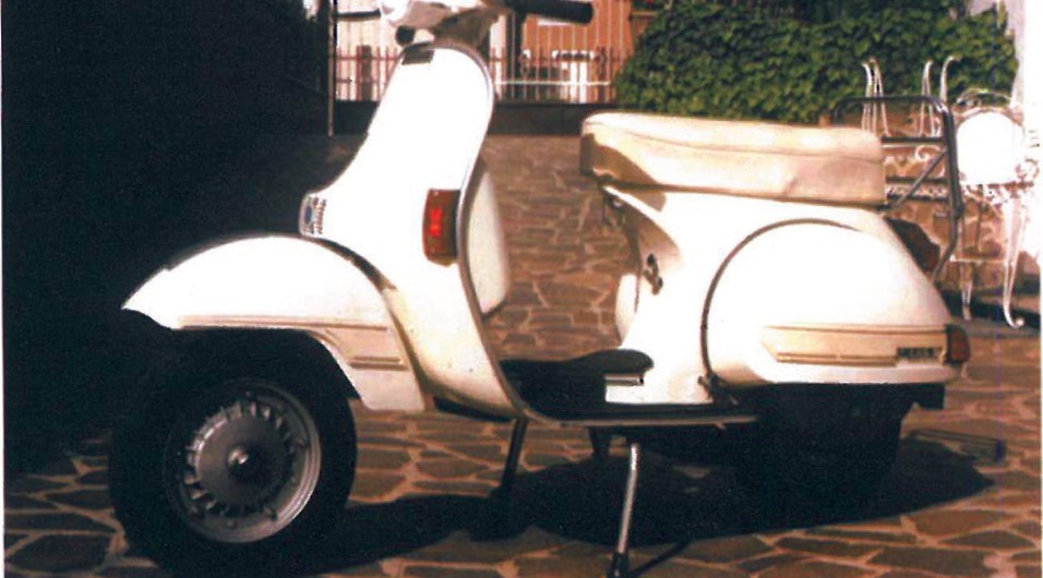 Light-grey Vespa PX scooter parked on a tiled patio with shutters in the background, a model familiar to Iranian riders