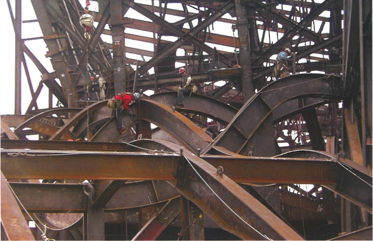 Workers walking across the dense lattice of curved steel members forming the three-dimensional structural net of the Walt Disney Concert Hall roof