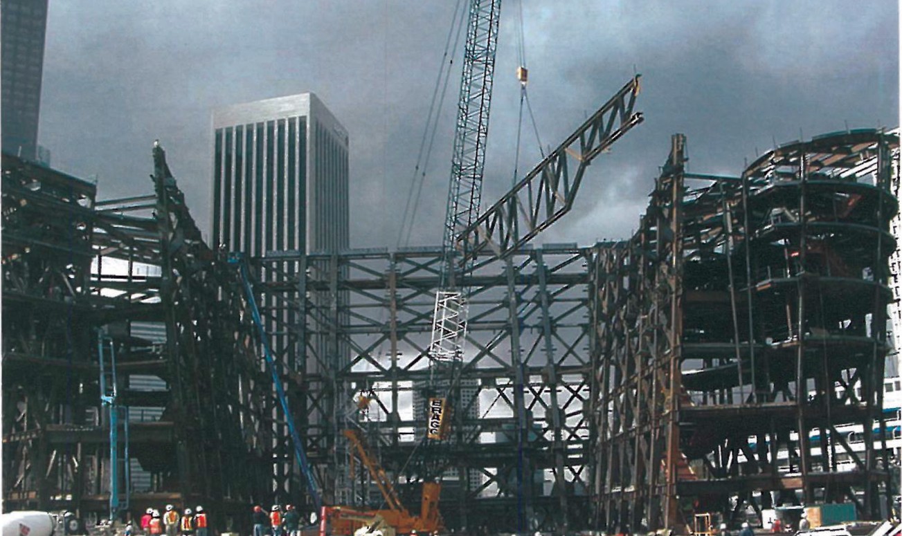 Construction site of the main steel structure of Walt Disney Concert Hall, a tower crane erecting curved trusses with workers gathered in the foreground