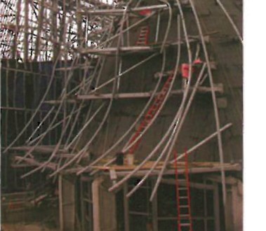 Curved tubular secondary frame with red and silver scaffold rising up the exterior of Walt Disney Concert Hall to support the metal facade panels
