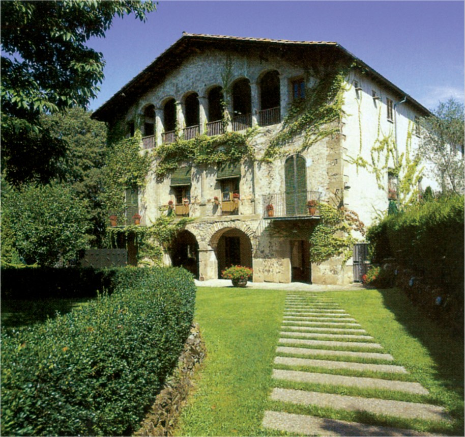 The 16th-century stone masia (farmhouse) housing Les Cols Restaurant, viewed from the garden with a path of stone slabs leading to the entrance