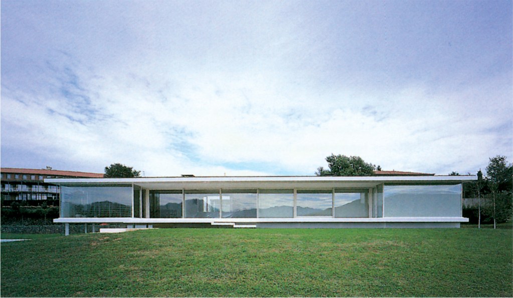 Casa Morales by RCR, a long horizontal glass pavilion set in a meadow with mountains in the distance