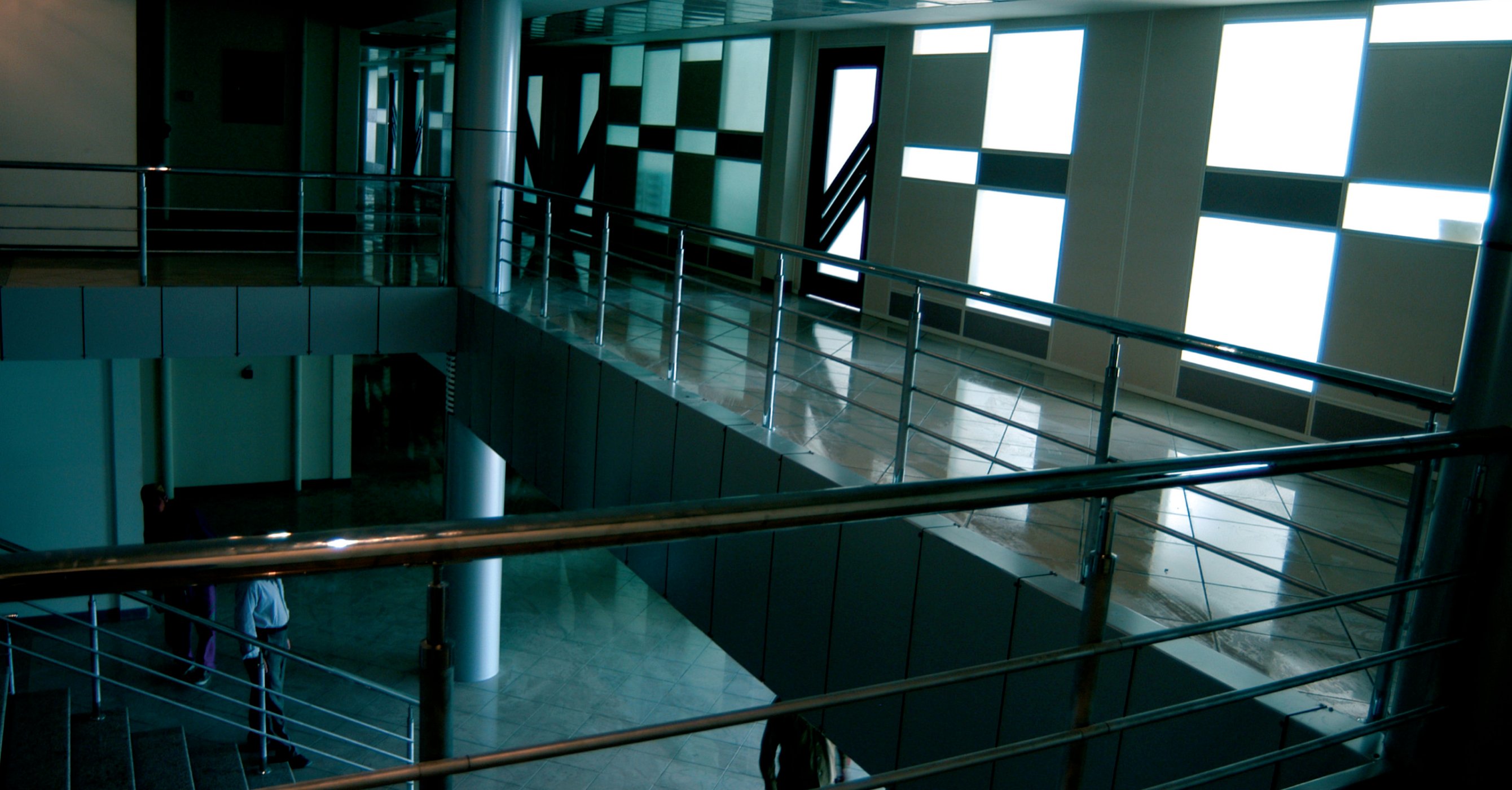 Interior view of the building's mezzanine: a staircase, metal railings and a black-and-white checkerboard tiled floor