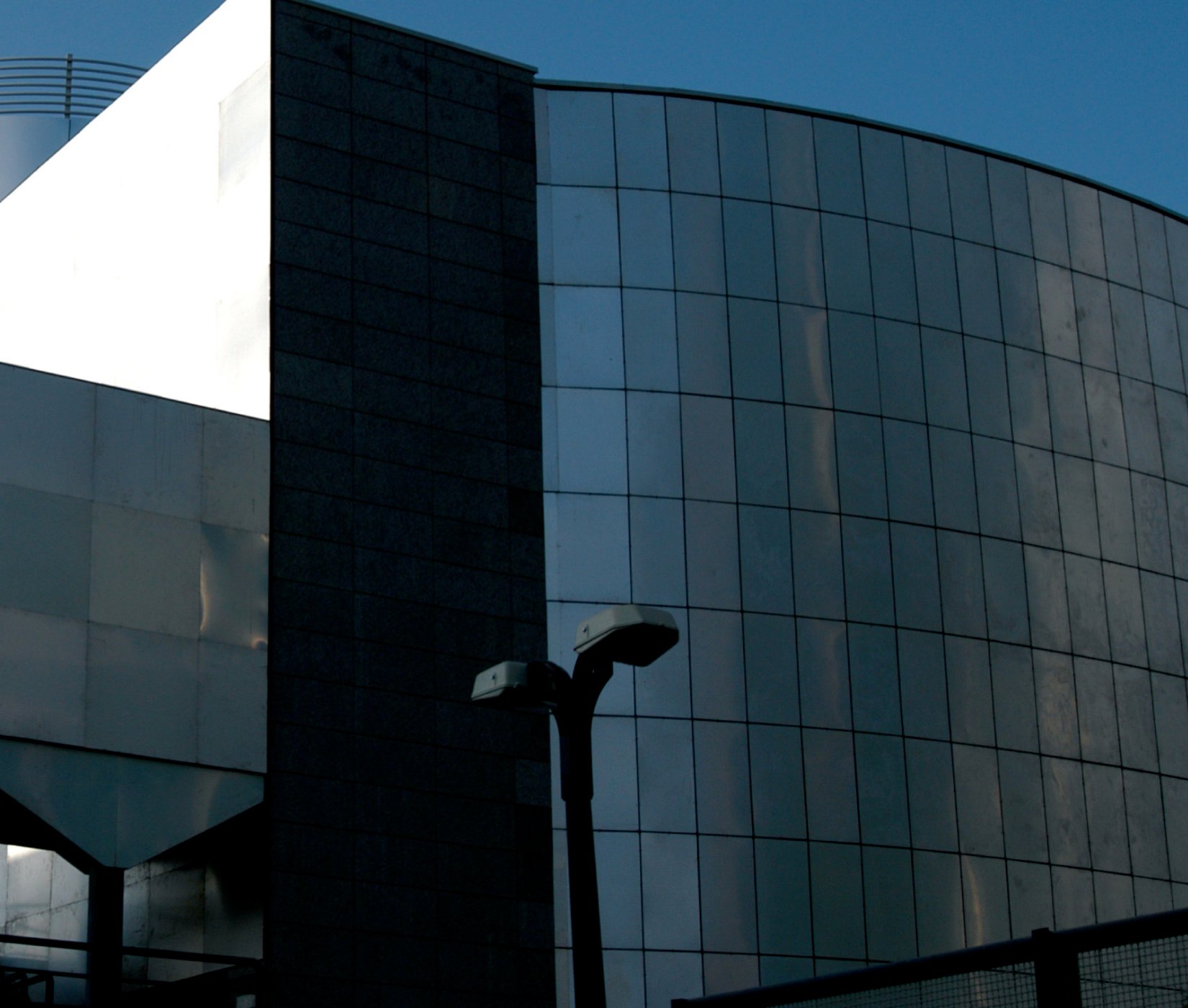Exterior of the Iran Gas Company Building in Shiraz, designed by Mehrdad Iravanian: a dark stone clad volume meeting a curved glazed enclosure