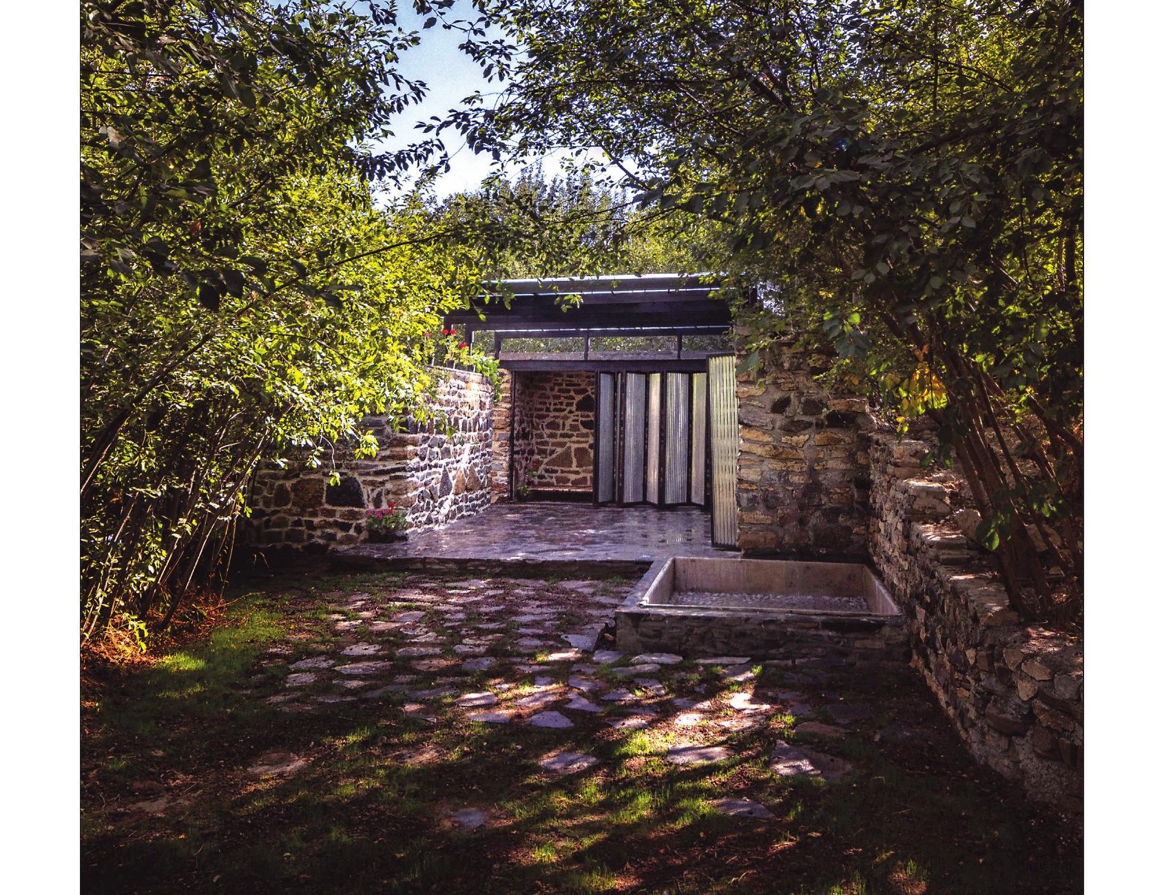 Stone-walled cabin glimpsed through orchard trees with paved entry court