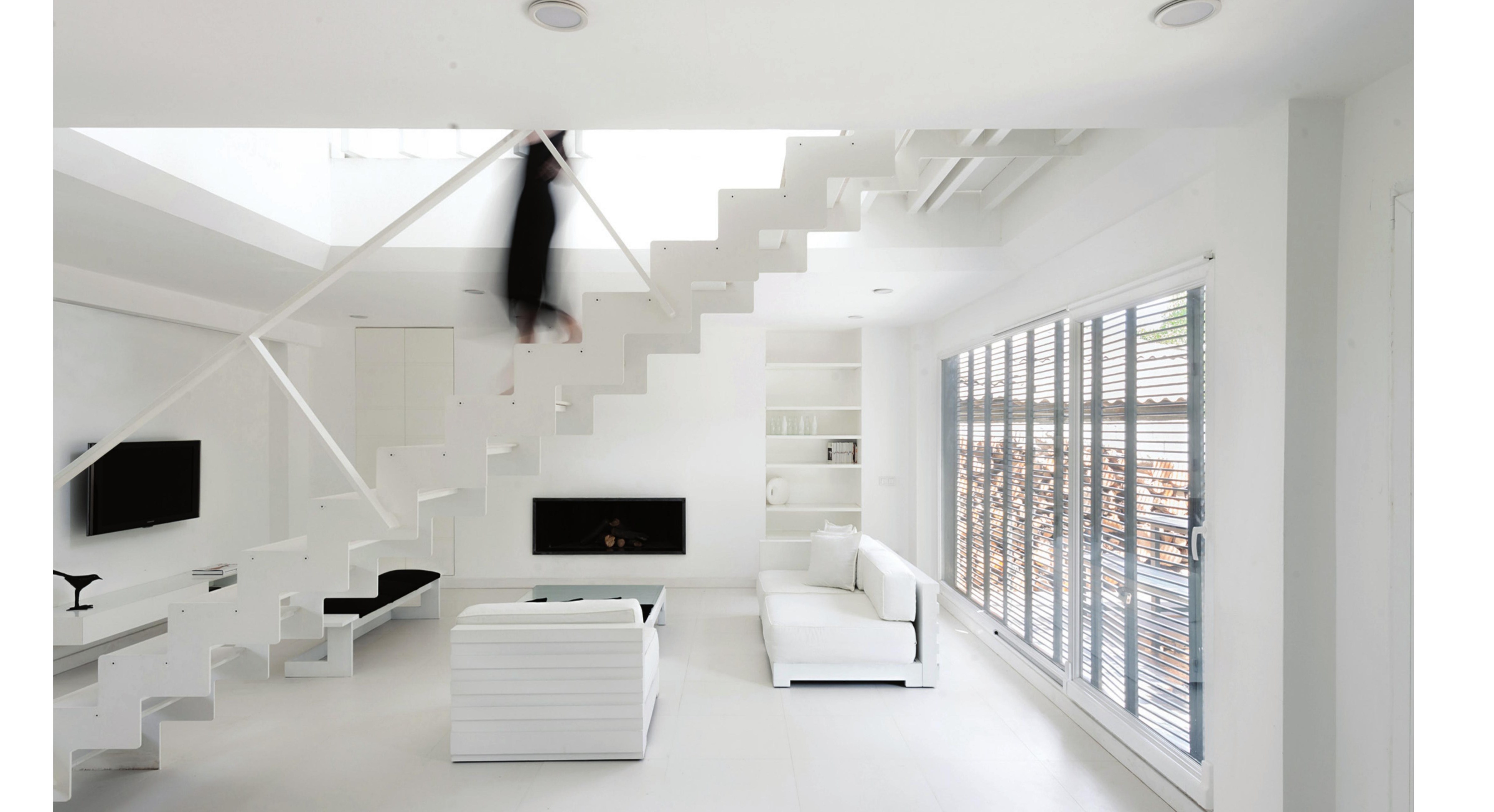Double-height living room: floating staircase, suspended slats, fireplace, and the louver-shuttered window facing the garden.