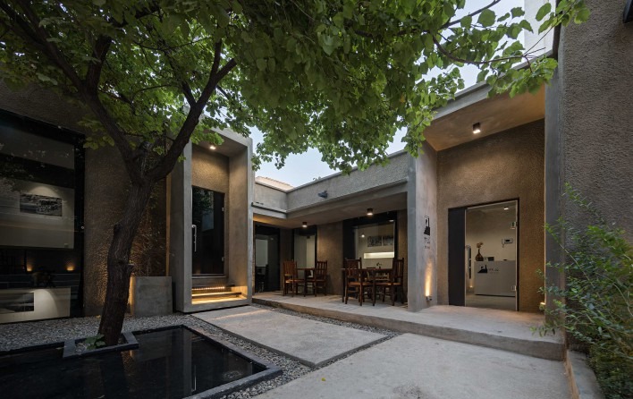 حیاط در شب‌گاه، اندکی دیرتر: نورِ تراسِ کافه و حوضِ کوچک زیرِ توت گرد آمده‌اند و کلِ خانه به مجموعه‌ای از اتاق‌هایِ سیمانی گردِ یک درخت خوانده می‌شود.