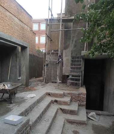 نمای میانه‌ی اجرایِ پلکانِ تازه: پاخورهای آجری که از حیاطِ قدیمی برمی‌آیند، خطی را نشانه می‌گذارند که بعدتر به پله‌ی سیمانیِ رو به گالریِ مرتفع بدل می‌شود.