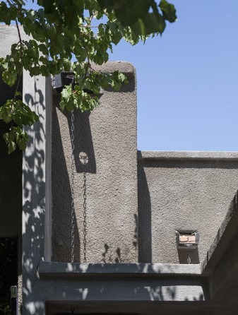 درگاهِ سیمانی با زنجیرِ بارش: آبِ بام به یک زنجیرِ بلند سپرده می‌شود و به ناودانیِ کوچکِ کنده‌کاری‌شده می‌رسد ـــ پاسخِ اقلیمی که، چنان که در شرحِ پروژه آمده، در دلِ سیمان نوشته شده است.