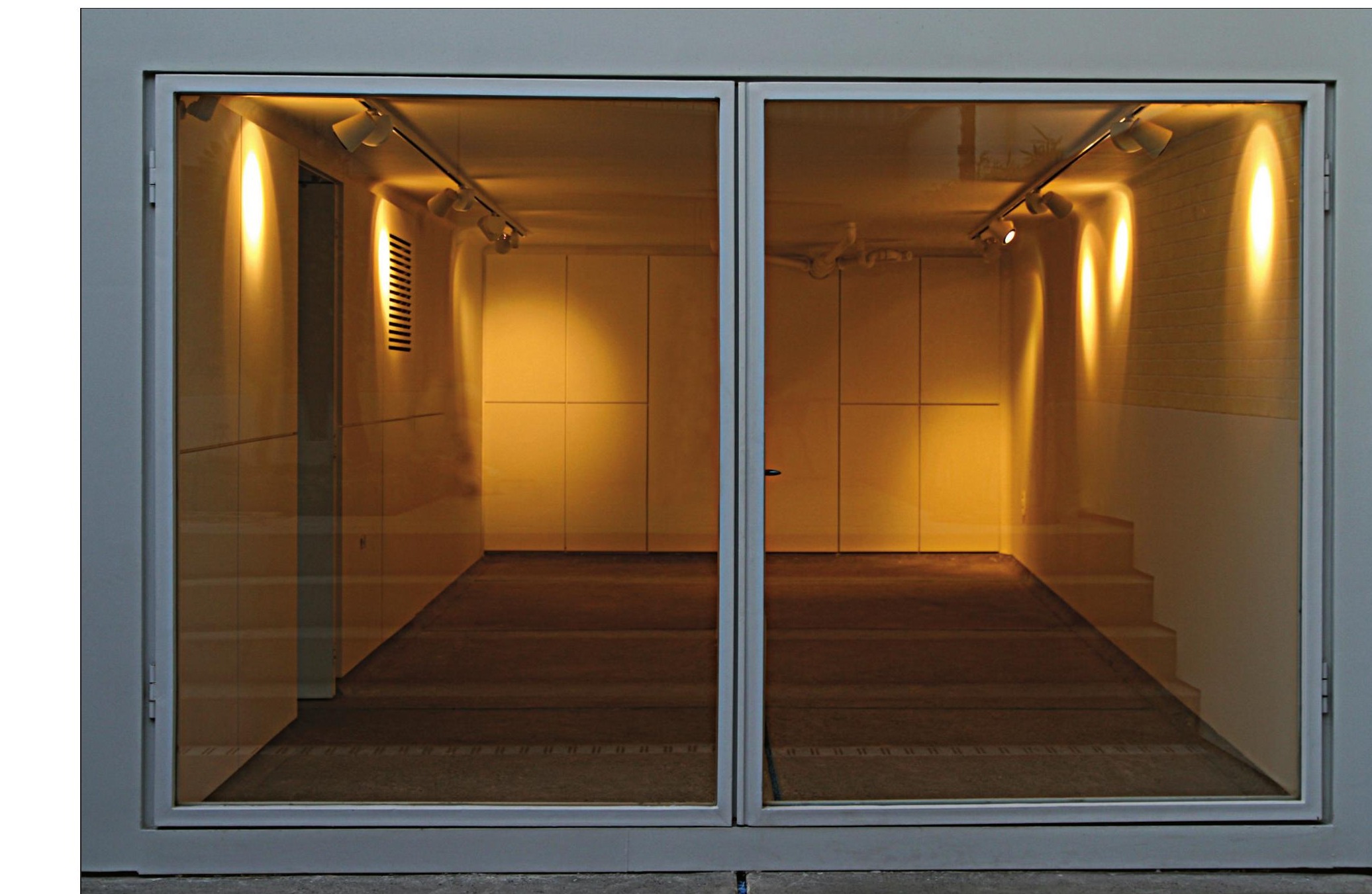 Gallery interior seen through large glass doors with track lighting
