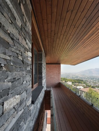 Side balcony detail with stacked stone wall on the left and brick chimney on the right under a wooden ceiling